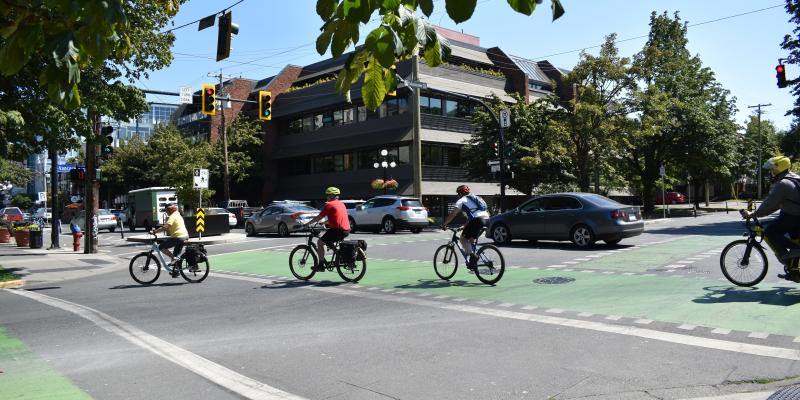 Cars and cyclists moving through a downtown intersection.