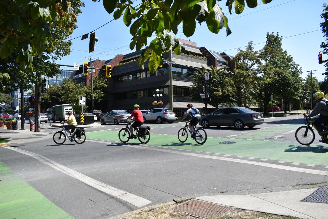Cars and cyclists moving through a downtown intersection.