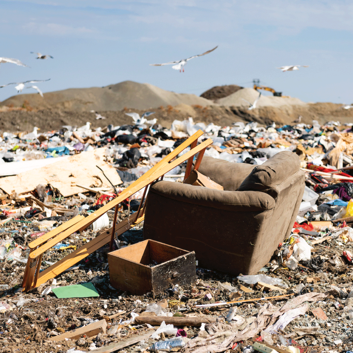 Armchair, broken ladder and drawer amongst landfill trash